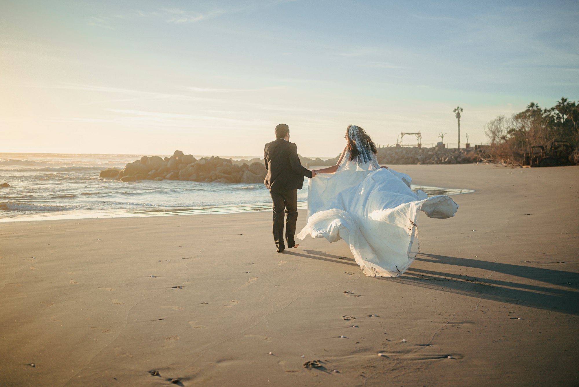 Bride and groom walking on the beach at sunset